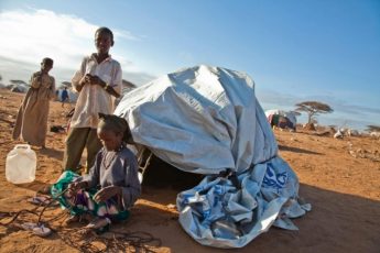 Fatuma Abdi Ali, a farmer from Dinsor Somalia weaves a cord to build her hut Dagahaley camp, Kenya as her son Jama Jalaf stands by. © UNHCR